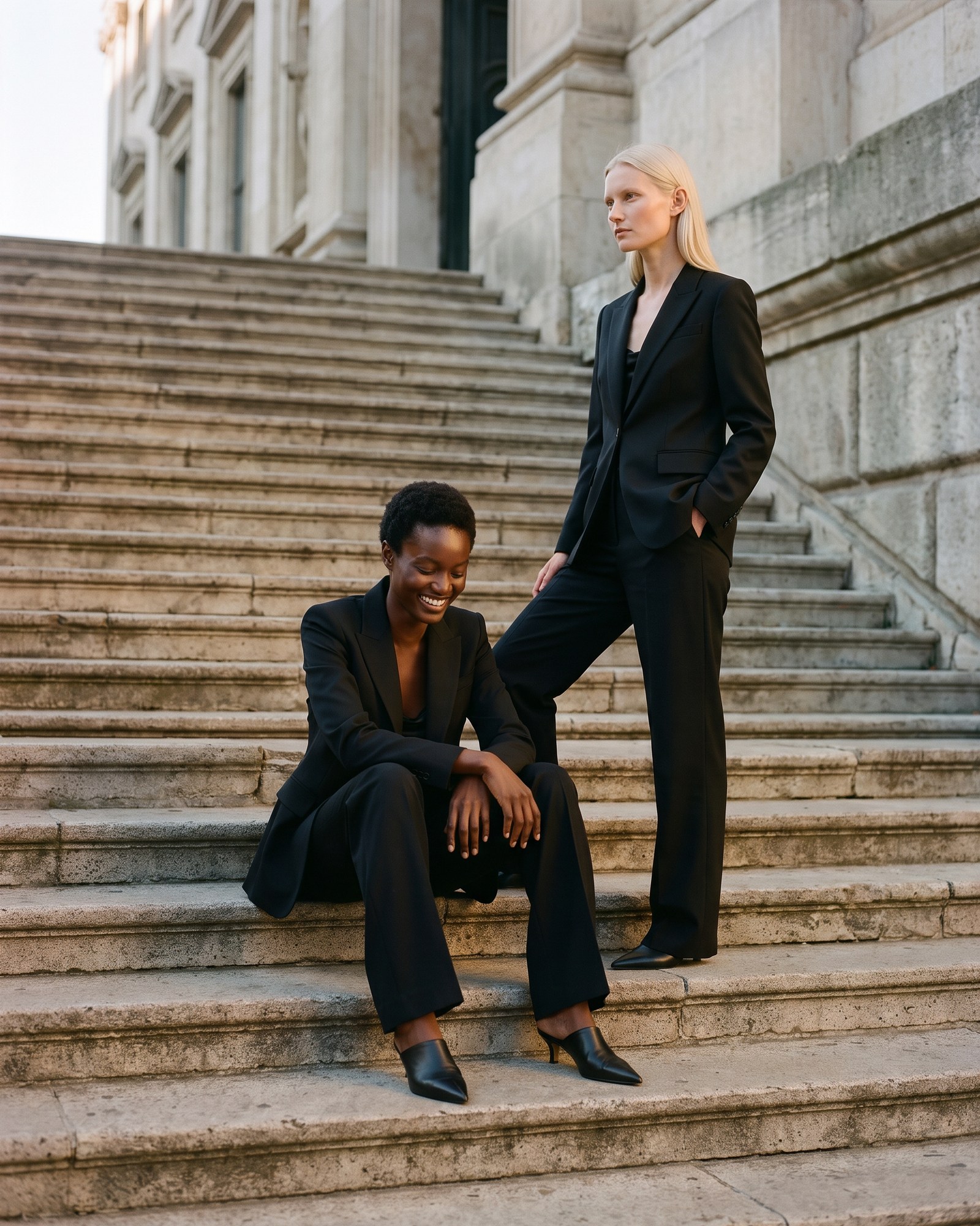 Two women in The Blazer and The Wide Trouser on the steps of an old stone building